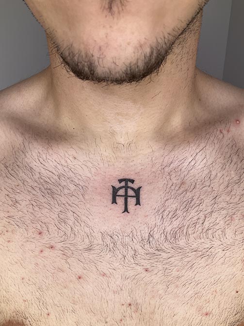 Tatuaje pequeño para hombre de una cruz o simbolofamiliar en el pecho