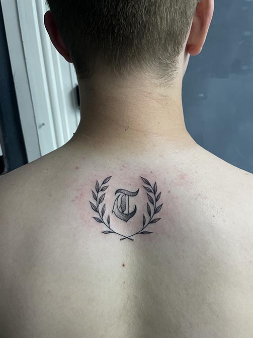 Tatuaje pequeño para hombre de una inicial en la espalda
