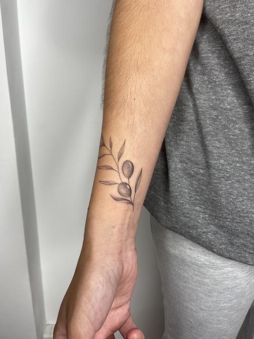 Tatuaje minimalista femenino de una rama de olivo pequeña para mujer en el antebrazo