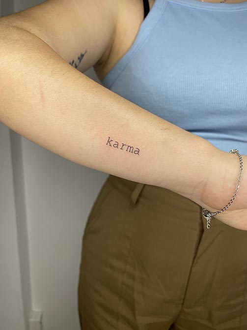 Tatuaje minimalista femenino de la palabra "Karma" pequeña para mujer en el antebrazo