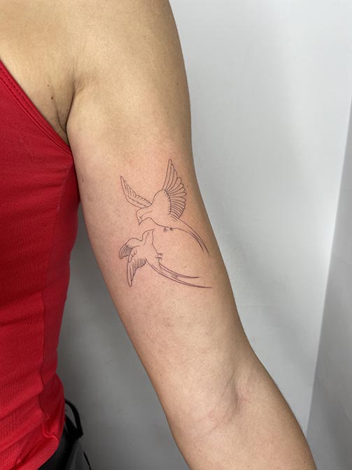 Tatuajes fine line de dos golondrinas volando en el brazo
