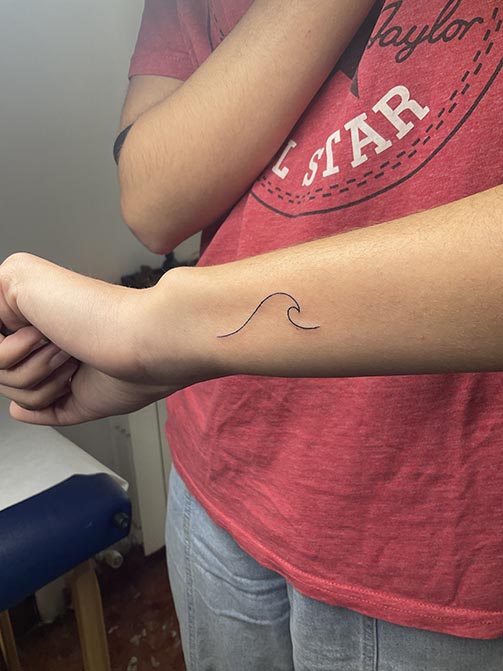 Tatuaje pequeño para mujer en el brazo estilo fineline de una ola