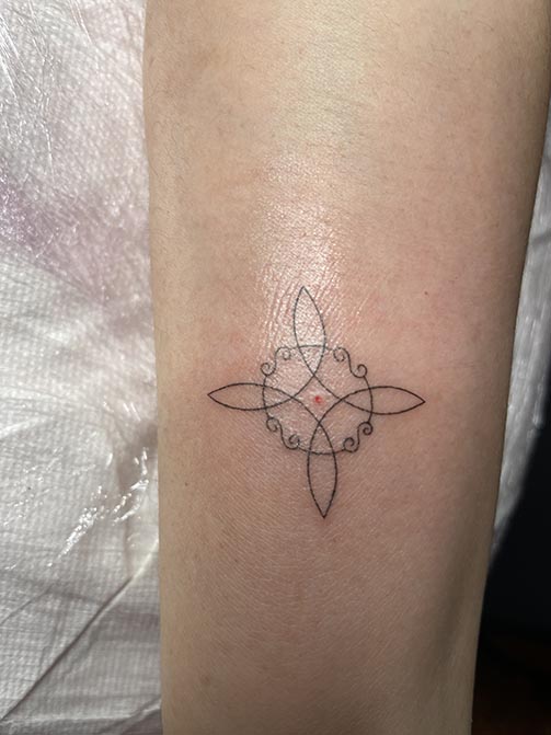 Tatuaje pequeño para mujer en el brazo del símbolo nudo de bruja