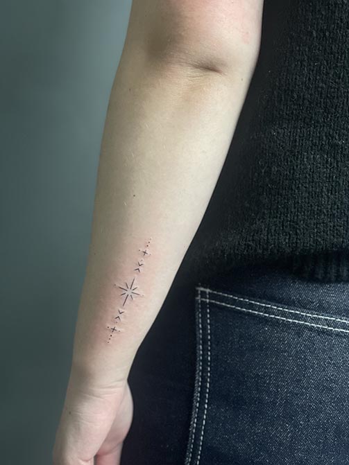 Tatuaje pequeño para mujer en el brazo con símbolos y estrellas