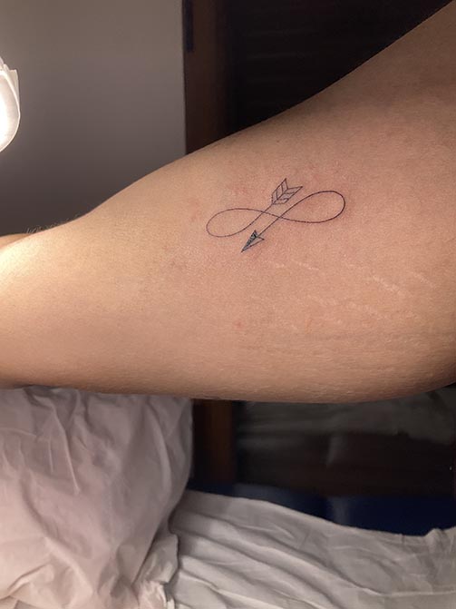 Tatuaje pequeño con significado para mujer  de un infinito con forma de flecha en el brazo